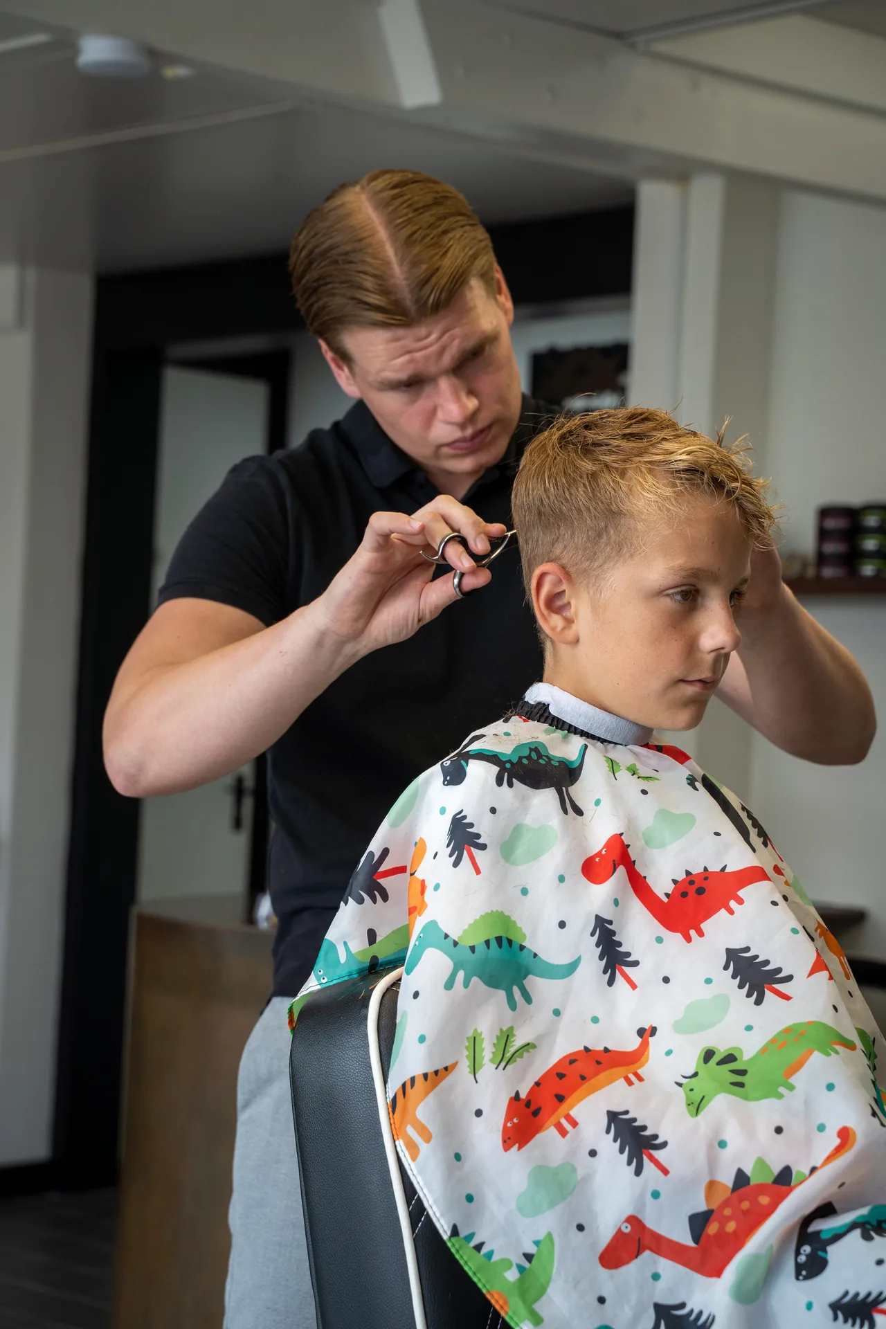 Een barber knipt een jonge klant in de stoel bij Barbershop Olle